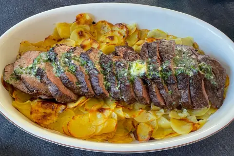 Skivat oxfile med örtsmör över krispiga potatisskivor. Ett perfekt oxfile recept för en festmåltid.