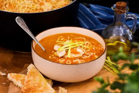 En skål med kycklingsoppa med nudlar och grönsaker, perfekt för ett enkelt kycklingsoppa recept. Serveras med rostat bröd och en flaska olivolja.