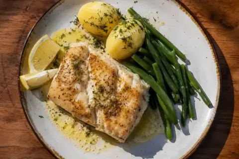 En tallrik med stekt torskrygg, kokt potatis, gröna bönor och citronklyftor.
