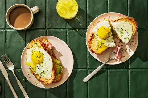 Två läckra croque madame med stekt ägg och avokado, serverade med kaffe och juice.