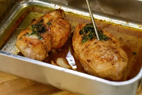 Två saftiga kycklingfiléer i ugnsform, redo för ett strimlad kyckling recept. En termometer mäter temperaturen.
