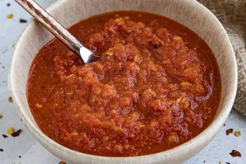 En skål med hemgjord chilisås, perfekt för ditt nästa chilisås recept. En sked i skålen visar den rika, kryddiga konsistensen.