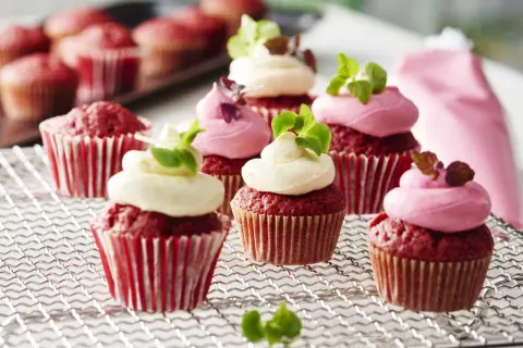 Red velvet cupcakes med fluffig frosting, perfekta för ett cupcakes recept. Garnerade med gröna blad och en rosa sprits.