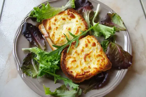 Två gyllene croque monsieur med smält ost och en fräsch sallad på en tallrik.