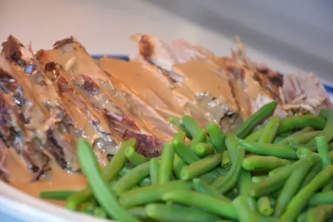 Skinkstek i gryta, saftig och uppskuren, serveras med en krämig sås och gröna bönor. En klassisk och smakrik rätt.