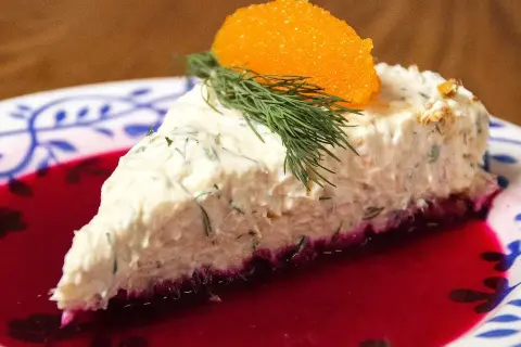 En bit lax cheesecake med dill och rom på en tallrik med rödbetsjuice.