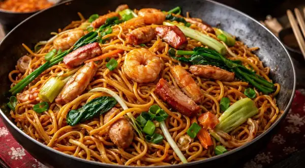 En stor portion chow mein med räkor, fläsk och grönsaker i en wok.