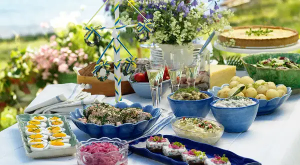En dukning med typisk svensk midsommarmat: sill, ägg, potatis, paj och en midsommarstång.