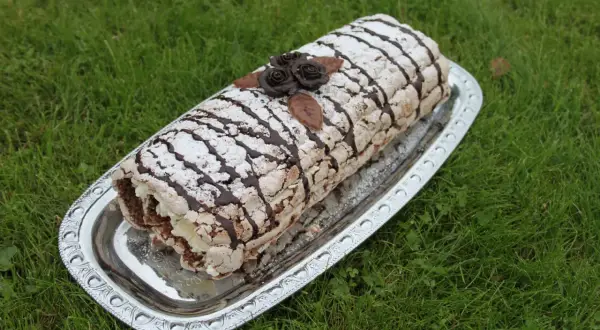 En läcker Budapestrulle med choklad och grädde, dekorerad med chokladrosor och pudersocker. Perfekt för ett sommarfika.