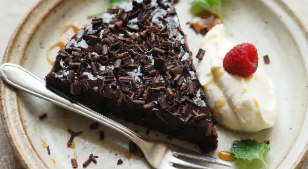 En bit kladdkaka med chokladtopping och hallon, serverad med grädde. Perfekt för dig som vill ha glutenfria kladdkakemuffins.