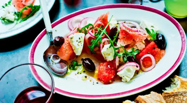 En uppfriskande melon och fetaostsallad med oliver, rödlök och ruccola, serverad på en tallrik med en sked.