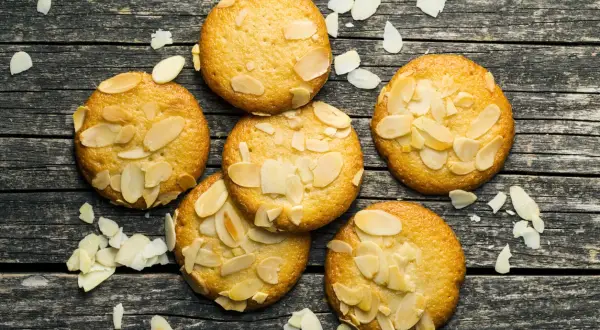 Sju gyllene bondkakor med mandelflagor på en mörk träyta. Perfekt för ditt bondkakor recept.