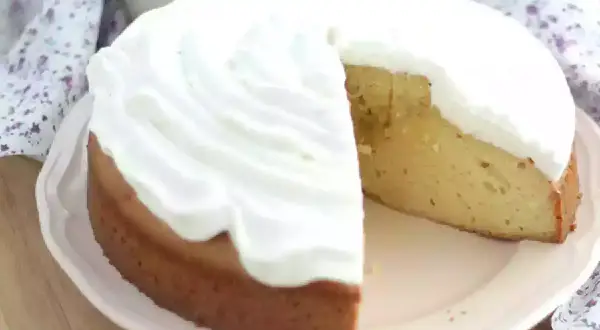 En saftig tres leches-kaka med fluffig grädde. En bit är bortskuren, vilket avslöjar den gyllene kakan.