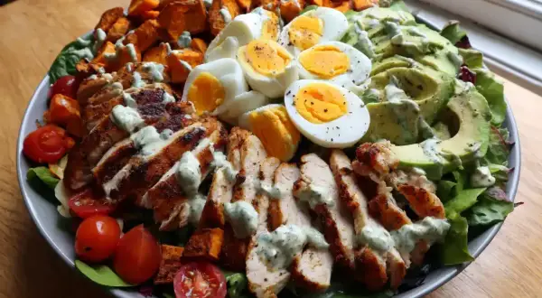 Enkel sallad med grillad kyckling, kokta ägg, sötpotatis, avokado och körsbärstomater, toppad med en krämig dressing.