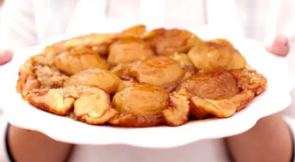 En gyllene tarte tatin med karamelliserade äpplen på en vit tallrik, redo att serveras.