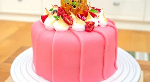 En vacker rosa prinsesstårta med marängtoppar, bär och en karamellkrona. Perfekt för ett prinsesstårta recept!