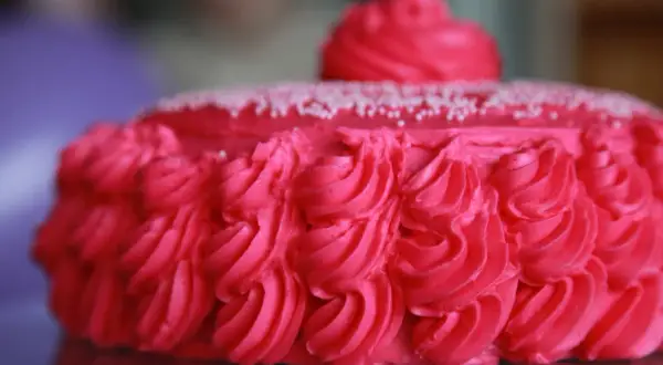 En vacker rosa tårta med rosettmönster i frosting och små vita strössel. Perfekt för ett firande!
