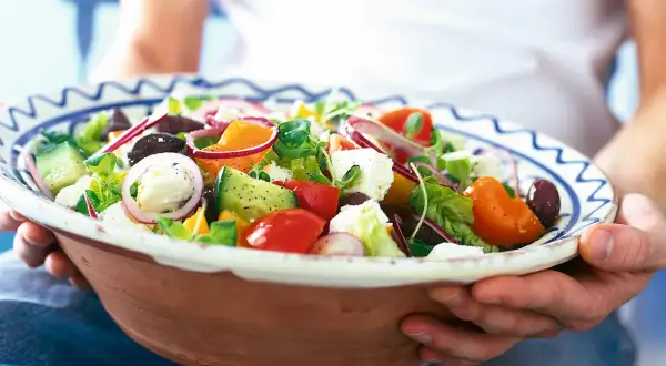 En stor skål med en god sallad till maten, full av färska grönsaker som tomat, gurka, paprika, lök och fetaost.