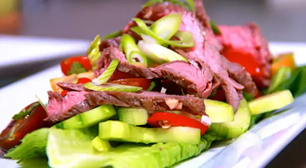 En läcker asiatisk biffsallad med tunt skivad biff, gurka, tomat och salladslök på en bädd av krispig sallad.