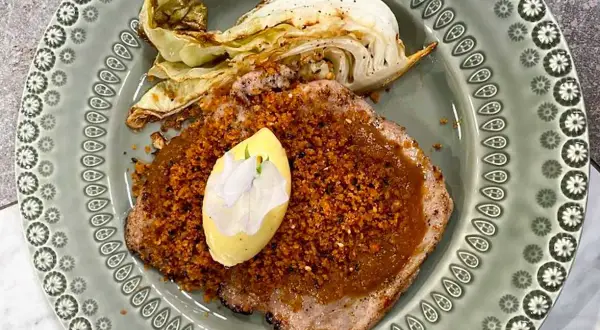 Schnitzel med krispigt täcke och en klick kall sås, garnerad med en blomma. Serveras med ugnsrostad kål.