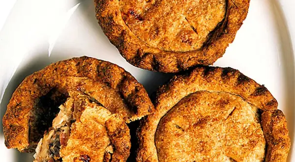 Tre gyllene små pajer på en vit tallrik. En paj är uppskuren och visar ett smakrikt innehåll. Perfekt för en fika!