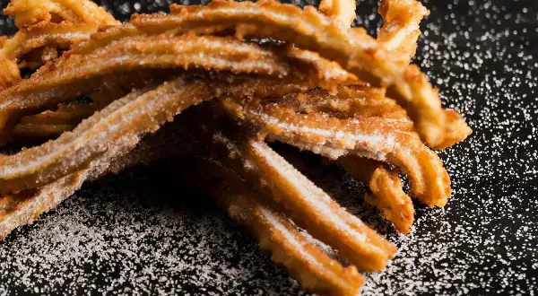 Krispiga churros, pudrade med socker, redo att avnjutas. Ett enkelt churros recept för hemmabruk.