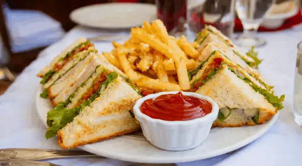 En tallrik med en klassisk club sandwich, pommes frites och ketchup. Perfekt för en lunch!