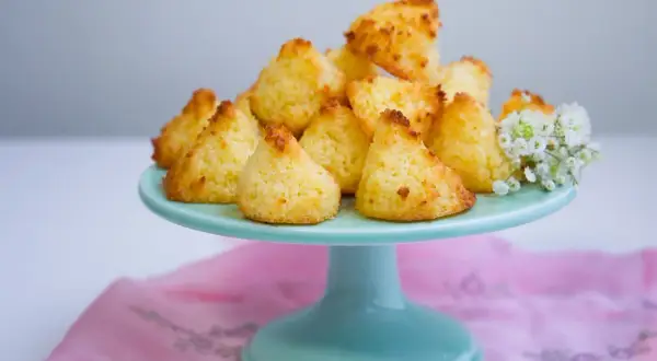 En hög med gyllene kokostoppar på ett turkost fat, redo att avnjutas. Ett enkelt kokostoppar recept som ger ljuvliga små bakverk.