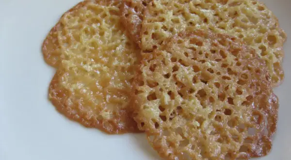Tre gyllene havreflarn utan sirap ligger på en vit tallrik. De är tunna och krispiga med ett vackert mönster av små hål.