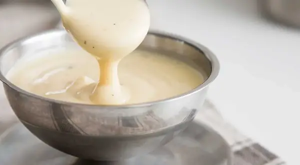 Krämig vaniljsås hälls upp ur en slev i en skål. Perfekt för ditt vaniljsås recept!