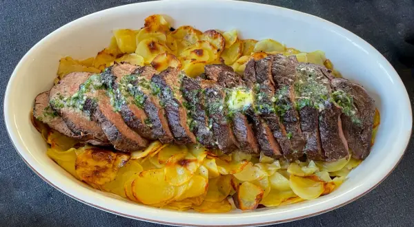 Skivat oxfile med örtsmör över krispiga potatisskivor. Ett perfekt oxfile recept för en festmåltid.