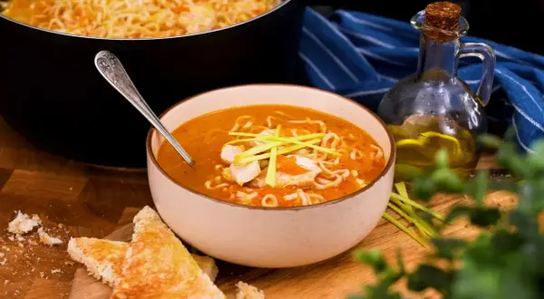 En skål med kycklingsoppa med nudlar och grönsaker, perfekt för ett enkelt kycklingsoppa recept. Serveras med rostat bröd och en flaska olivolja.