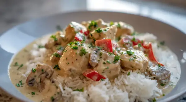 En krämig chicken a la king med ris, toppad med persilja och bitar av röd paprika.