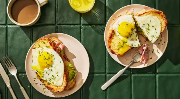 Två läckra croque madame med stekt ägg och avokado, serverade med kaffe och juice.