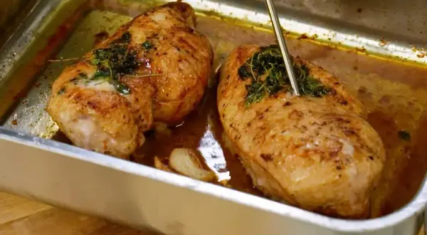 Två saftiga kycklingfiléer i ugnsform, redo för ett strimlad kyckling recept. En termometer mäter temperaturen.