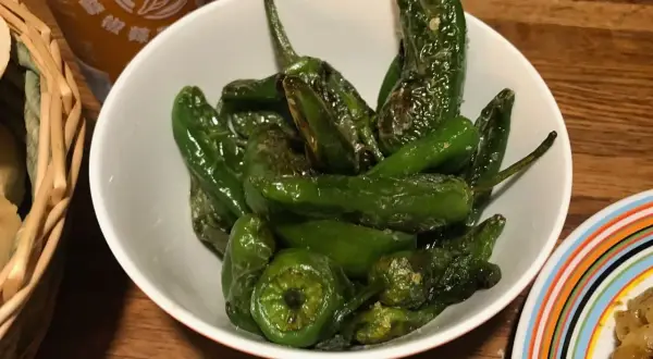 En skål med stekta pimientos de padron, glansiga och gröna, redo att avnjutas.