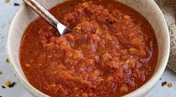 En skål med hemgjord chilisås, perfekt för ditt nästa chilisås recept. En sked i skålen visar den rika, kryddiga konsistensen.