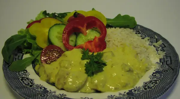En tallrik med kyckling curry, ris och en sallad av paprika, gurka och tomat.