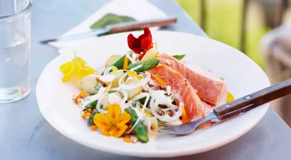 En läcker potatissallad med sparris och lax, dekorerad med ätbara blommor. Perfekt för en somrig lunch utomhus.