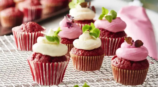 Red velvet cupcakes med fluffig frosting, perfekta för ett cupcakes recept. Garnerade med gröna blad och en rosa sprits.