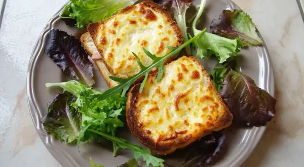 Två gyllene croque monsieur med smält ost och en fräsch sallad på en tallrik.