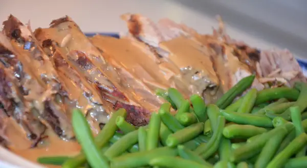 Skinkstek i gryta, saftig och uppskuren, serveras med en krämig sås och gröna bönor. En klassisk och smakrik rätt.