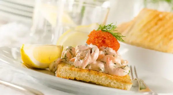 En perfekt toast skagen med krämiga räkor, rom och dill, serverad med citronklyfta. En riktig delikatess!