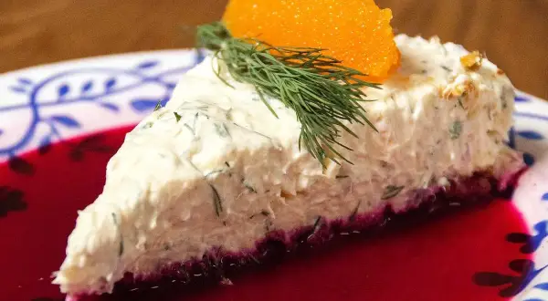 En bit lax cheesecake med dill och rom på en tallrik med rödbetsjuice.