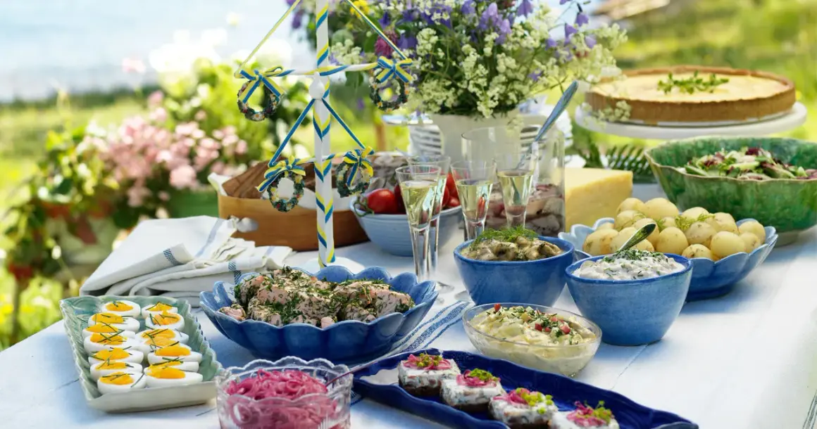 En dukning med typisk svensk midsommarmat: sill, ägg, potatis, paj och en midsommarstång.