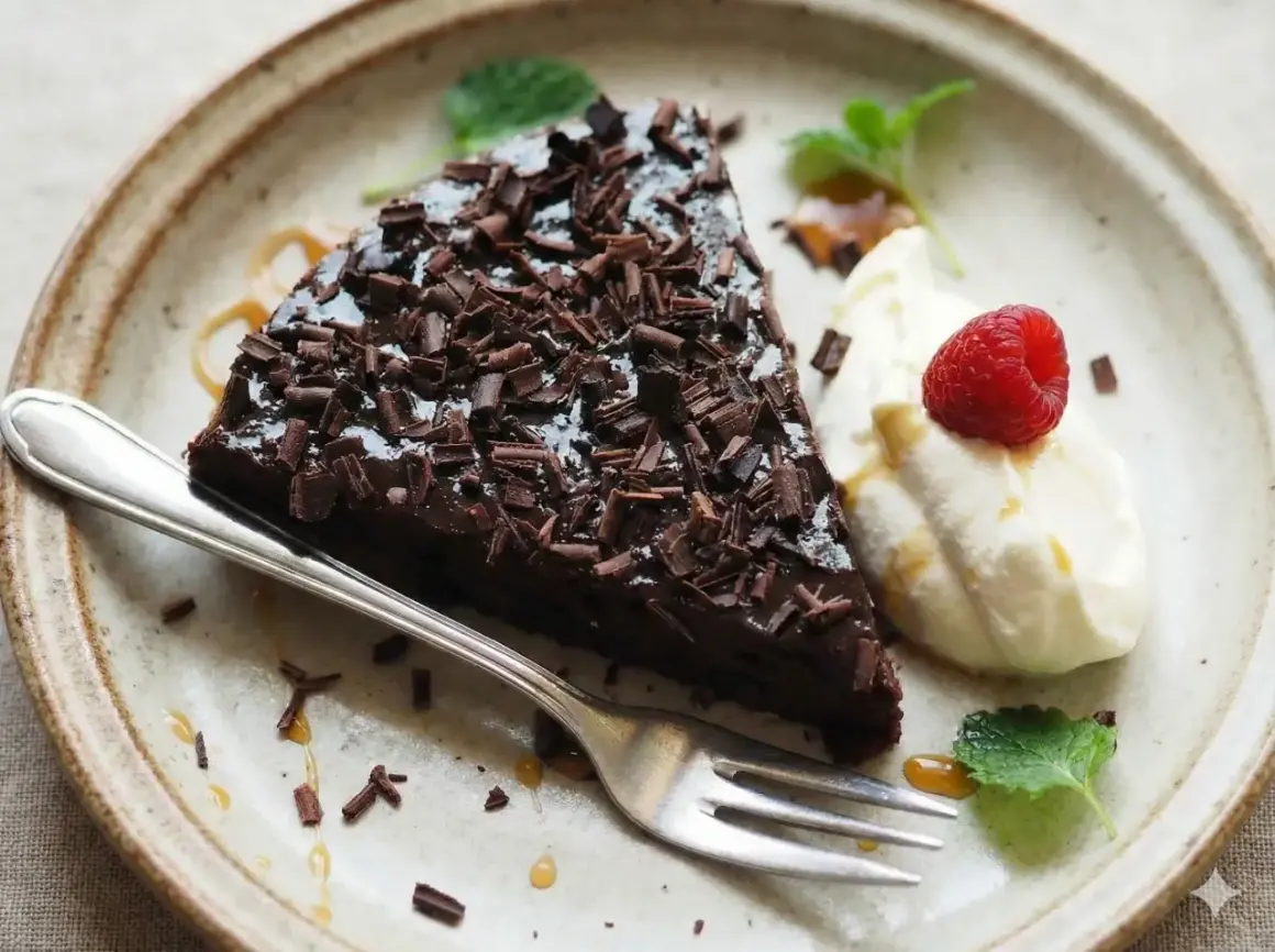 En bit kladdkaka med chokladtopping och hallon, serverad med grädde. Perfekt för dig som vill ha glutenfria kladdkakemuffins.