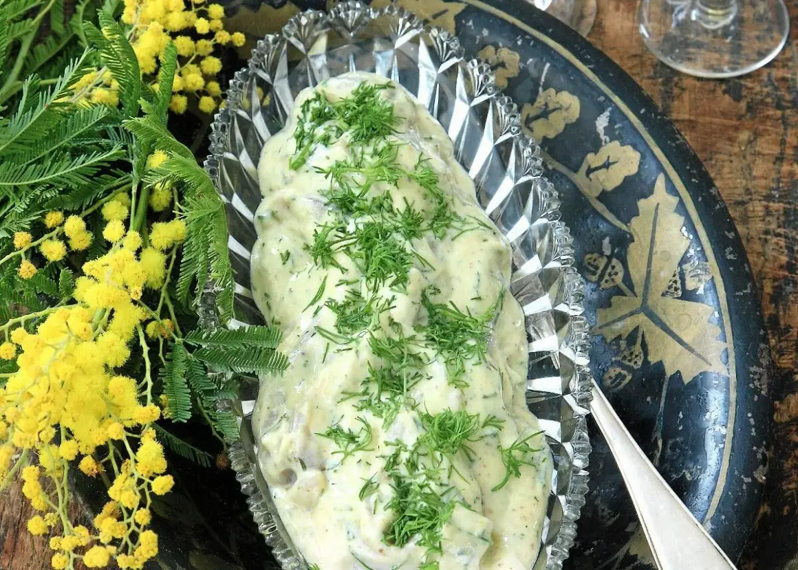 Krämig senapssill i en vacker skål, garnerad med dill. Bredvid syns gula mimosa-blommor. Ett perfekt senapssill recept för festen!