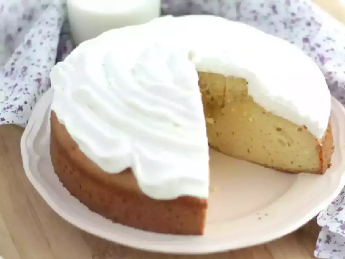 En saftig tres leches-kaka med fluffig grädde. En bit är bortskuren, vilket avslöjar den gyllene kakan.