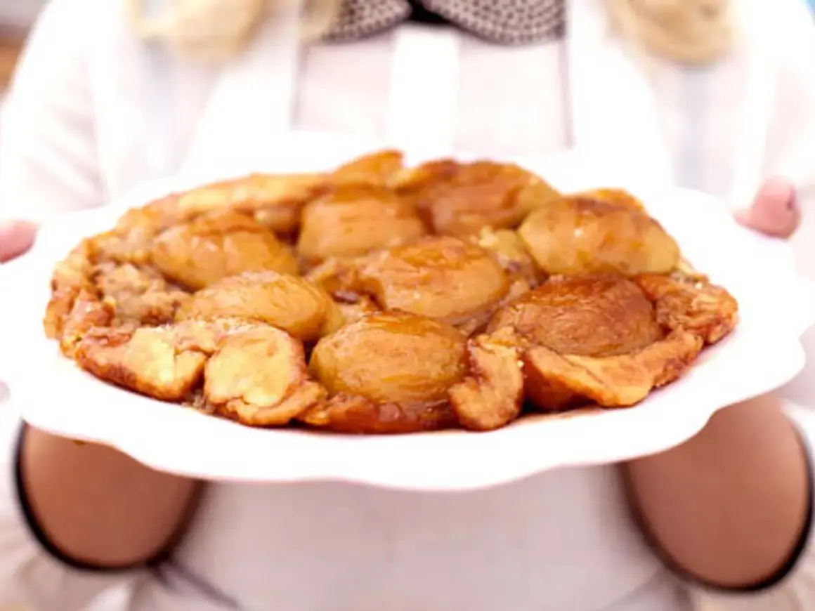 En gyllene tarte tatin med karamelliserade äpplen på en vit tallrik, redo att serveras.