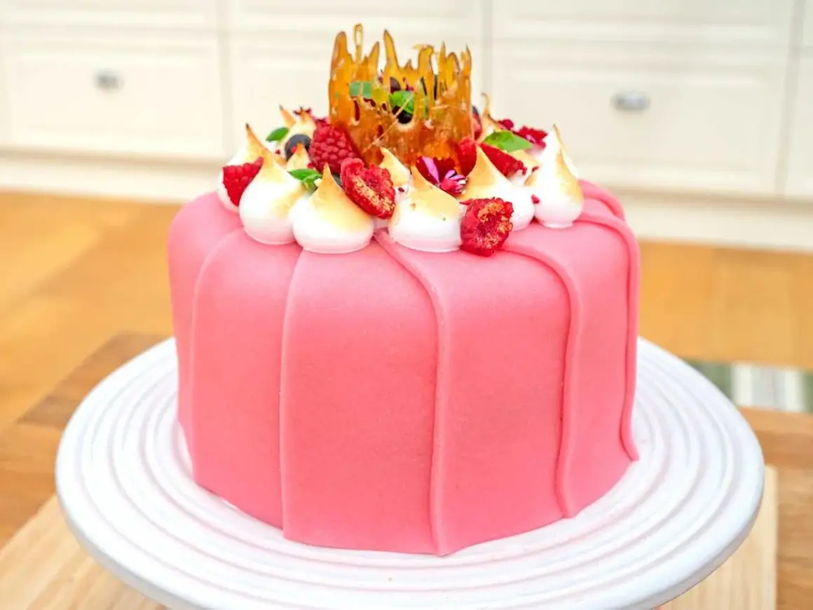 En vacker rosa prinsesstårta med marängtoppar, bär och en karamellkrona. Perfekt för ett prinsesstårta recept!
